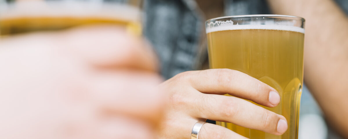 Person with wedding ring holding golden pint of non-alcoholic beer