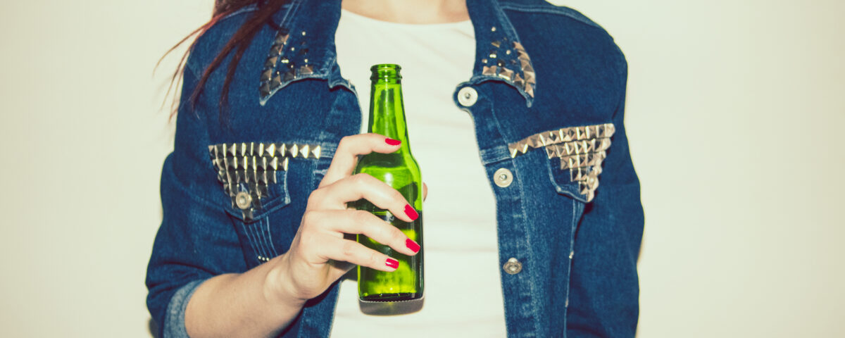 Young woman wearing a jean jacket, holding a non-alcoholic beer