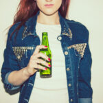 Young woman wearing a jean jacket, holding a non-alcoholic beer
