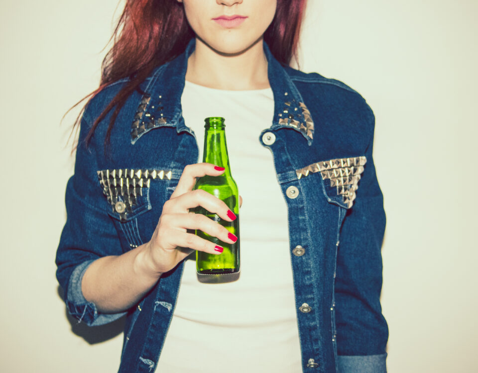 Young woman wearing a jean jacket, holding a non-alcoholic beer