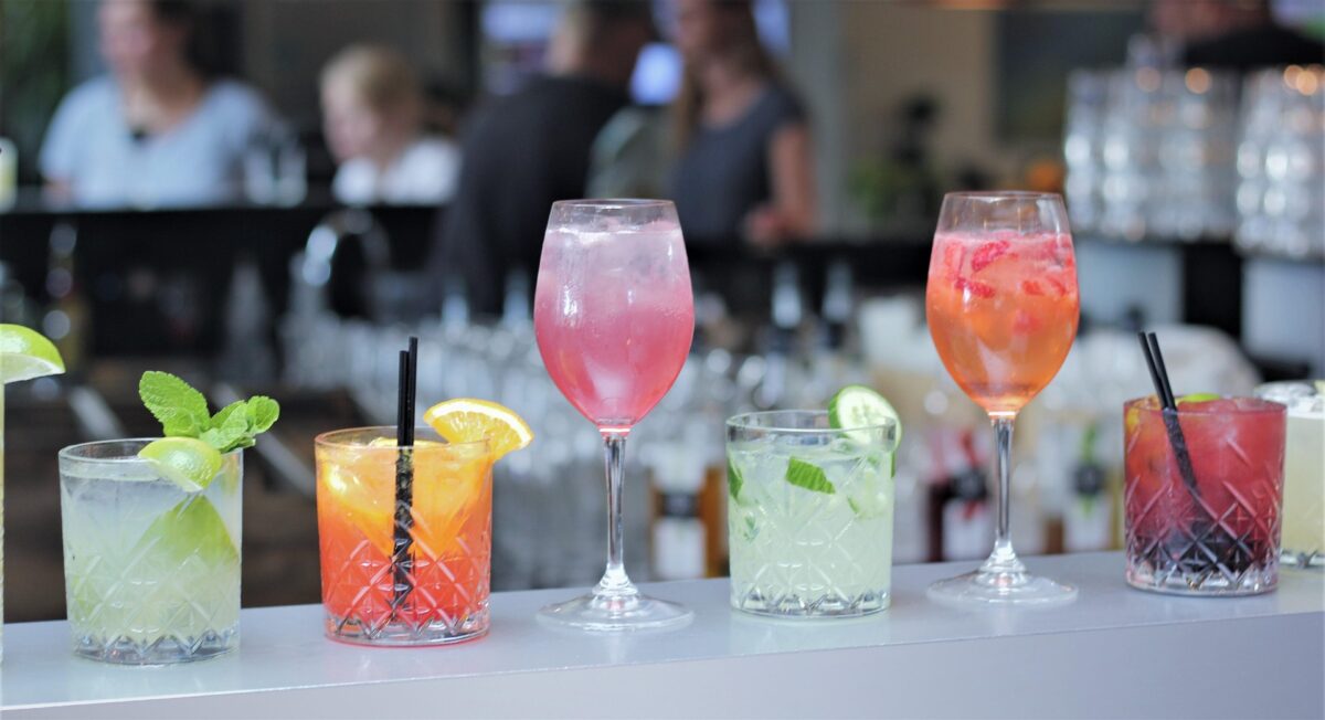 Image shows several glasses full of mocktails arranged on a bar in various drinkware.