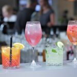 Image shows several glasses full of mocktails arranged on a bar in various drinkware.