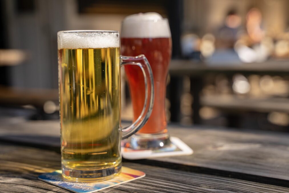 Image shows a stein of pale N/A beer on a table with a large glass of amber N/A beer behind it. Both sit on napkins.