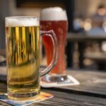 Image shows a stein of pale N/A beer on a table with a large glass of amber N/A beer behind it. Both sit on napkins.