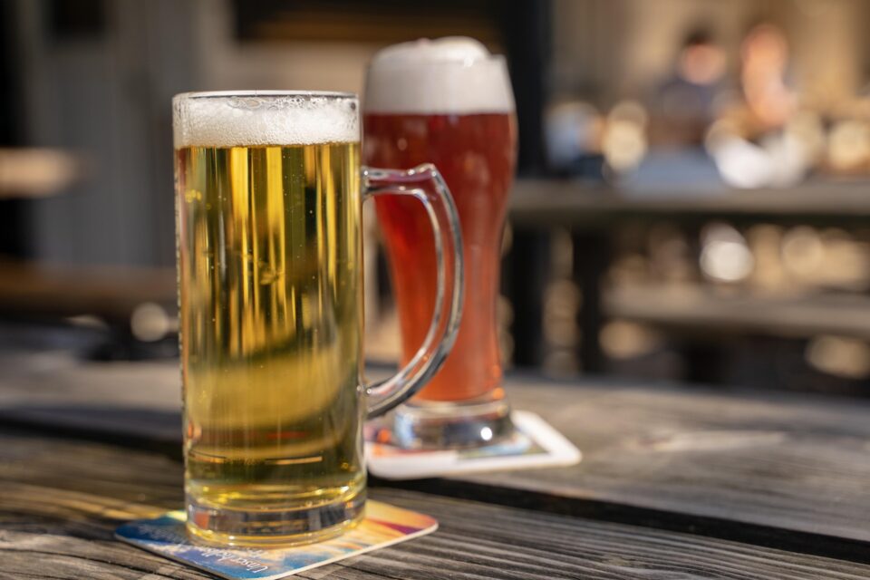 Image shows a stein of pale N/A beer on a table with a large glass of amber N/A beer behind it. Both sit on napkins.