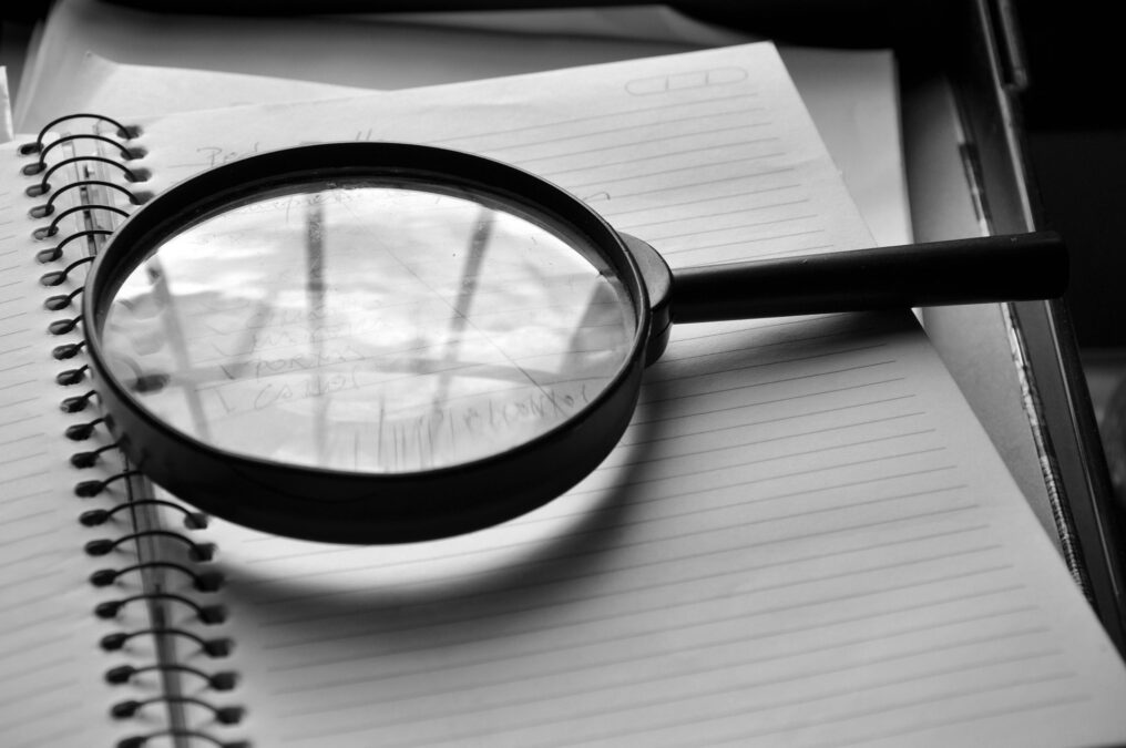 Image shows a magnifying glass resting on a spiral notebook.